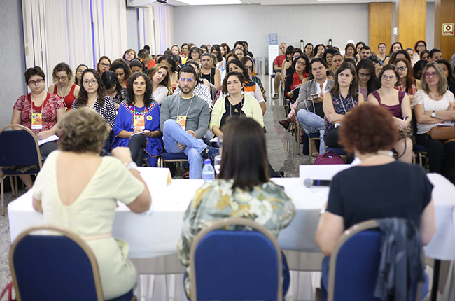 Imagem mostra participantes sentados/as e atentos/as, assistindo a uma palestra do Seminário