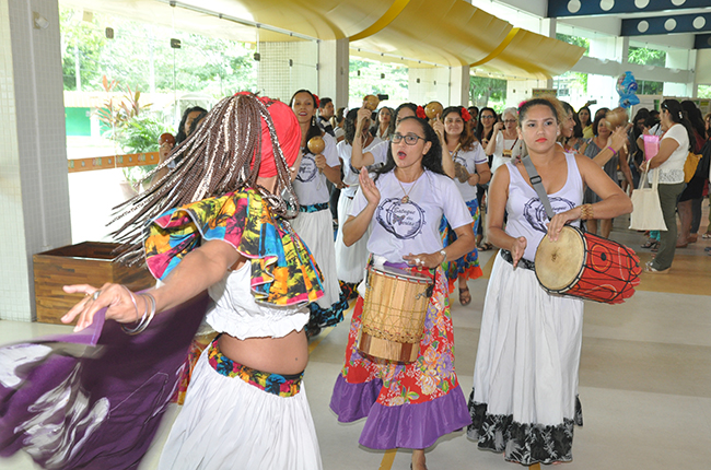 Foto mostra as integrantes do grupo As Marias segurando tambores e dançando