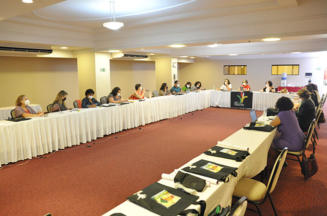 Imagem mostra a mesa completa com as convidadas do Seminário Latino-Americano reunidas com o CFESS e a Abepss antes do evento, em mesa com formato de U.