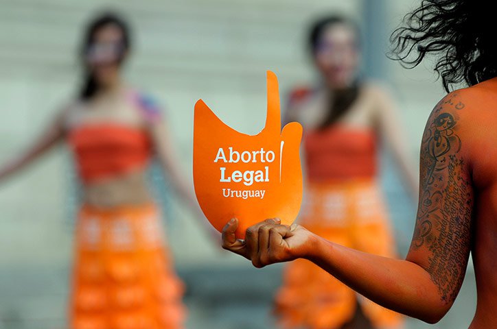 Imagem mostra mulher segurando cartaz com os dizeres Aborto legal Uruguai