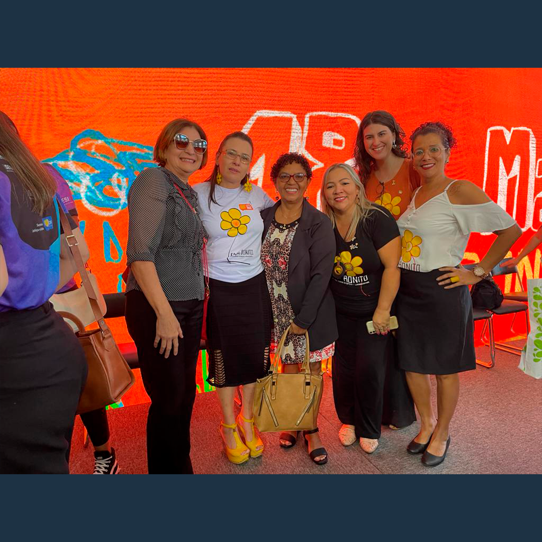 Imagem com telão laranja ao fundo mostra representantes do CFESS e do CRESS-DF em pé, durante evento alusivo ao Dia 18 de maio - Combate ao abuso e exploração sexual de crianças e adolescentes.
