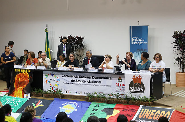 Imagem mostra mesa da audiência pública, durante a fala da professora Berenice Rojas.