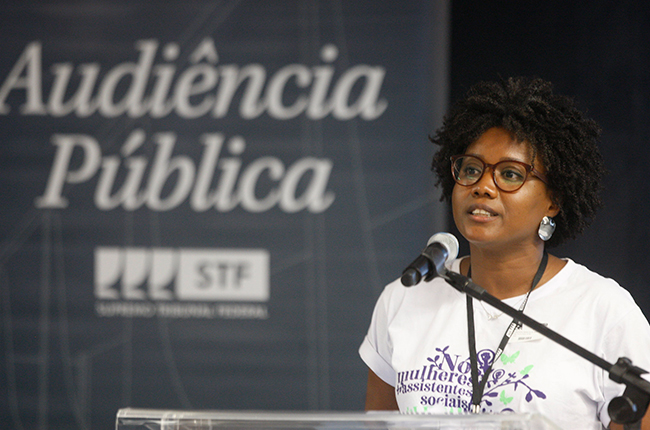 Imagem mostra a conselheira do CFESS Dilma Franclin em pé, durante seu momento de fala na audiência.
