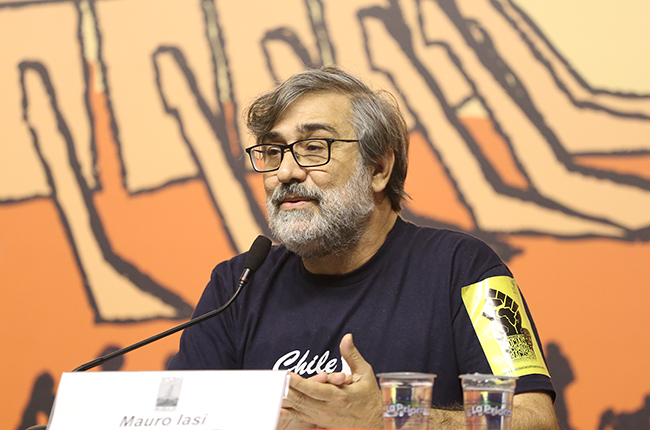 Foto do palestrante Maurio Iasi, de barba grisalha e óculos, falando para o público 
