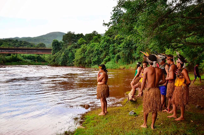 Imagens de indígenas em frente ao Rio Paraopeba, poluído com a lama tóxica de rejeitos.