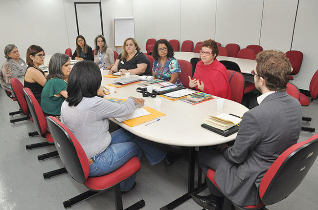 Imagem do grupo que foi até o MEC, sentado ao redor da mesa de reuniões, no momento em que a conselheira do CFESS Daniela Castilho fala.