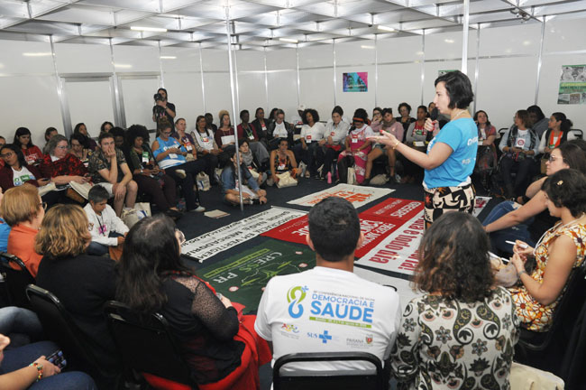 Imagem da reunião com assistentes sociais, reunidas em círculo, com a conselheira do CFESS Elaine Pelaez em pé falando.