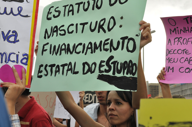 Foto de jovem segurando cartaz com os dizeres: Estatuto do Nascituro - financiamento estatal do estupro