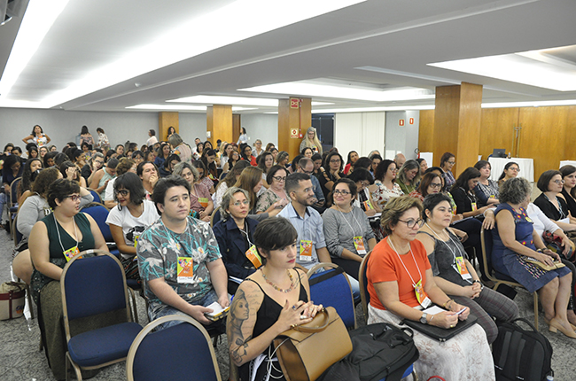 Imagem do auditório com cerca de 60 pessoas assistindo à mesa de debate