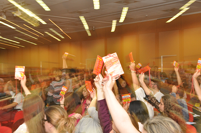 Imagem de participantes do evento com crachás levantados, no momento da votação