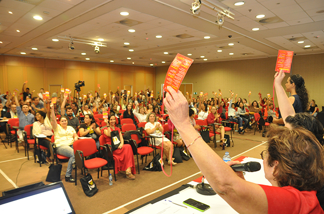 Imagem mostra plenária com participantes levantando seus crachás 