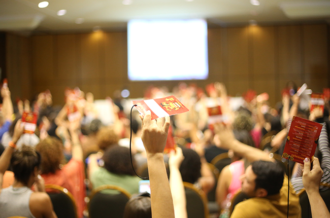Fotografia mostra participantes durante a plenária final, erguendo o crachá vermelho para aprovar as deliberações do Encontro