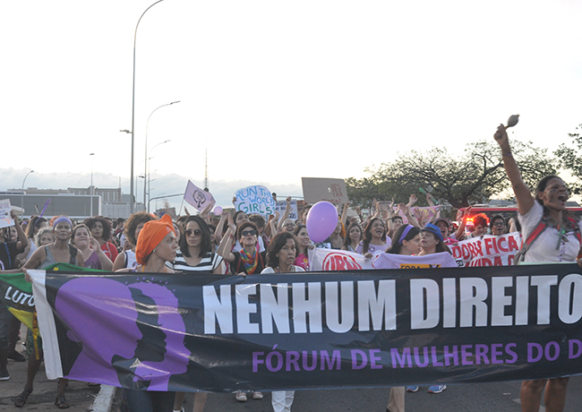 Imagem mostra mulheres levantando bandeiras com dizeres de luta caminhando em direção ao Congresso Nacional
