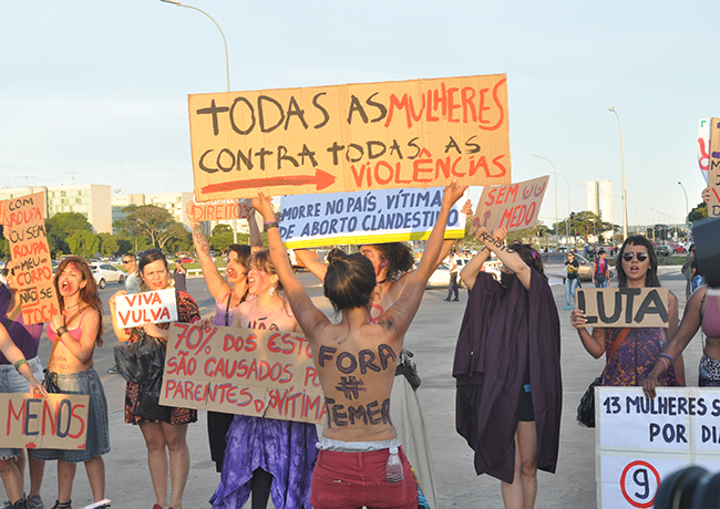 Imagem mostra mulheres segurando faixas denunciando a violência de gênero
