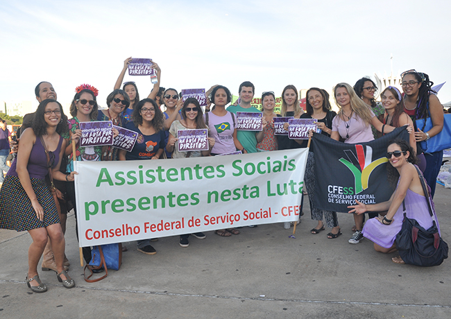 Foto mostra assistentes sociais e estudantes de Serviço Social com a faixa com os dizeres assistentes sociais nesta luta
