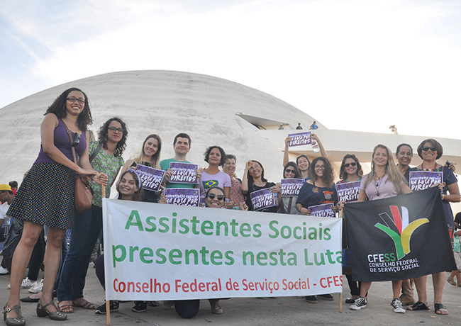 Foto mostra assistentes sociais juntas próximas à faixa do CFESS e com o Museu Nacional ao fundo