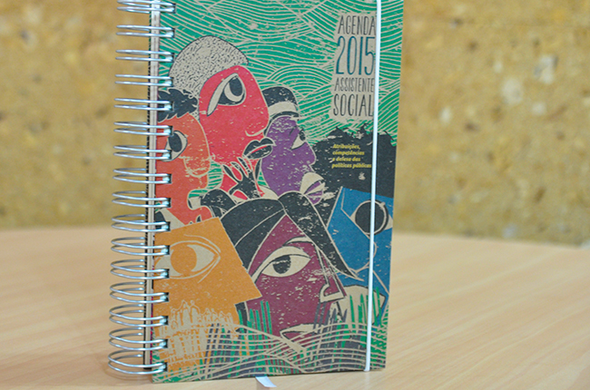 Foto mostra imagem da capa da Agenda 2015, em tons de verde-água, figuras humanas coloridas em traços rústicos