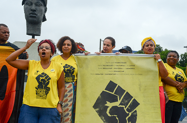 Imagem mostra a presidente do CFESS Josiane Soares, ao lado da presidente do CRESS-RJ, Dácia Teles, em fala em frente ao busto em homenagem a Zumbi