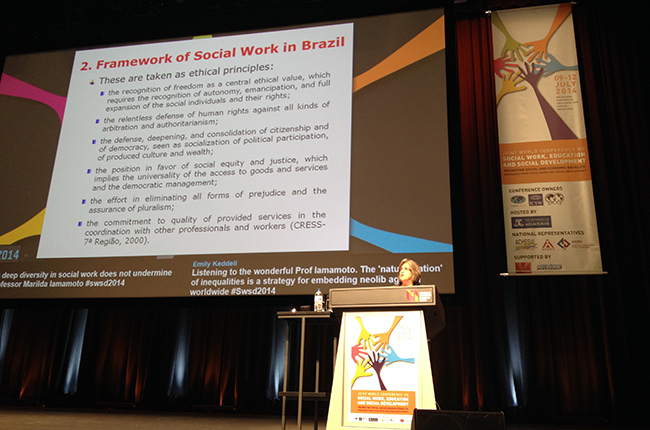 Imagem mostra professora Marilda Iamamoto palestrando durante Conferência Mundial