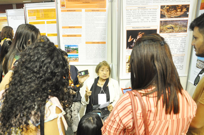 Imagem mostra professora Joaquina Barata falando de sua pesquisa para participantes do evento.