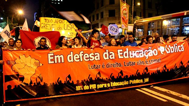 Imagem mostra ato político nas ruas do Rio de Janeiro. Manifestantes seguram faixa com dizeres em defesa da educação pública