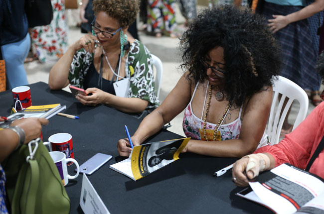 Imagem mostra autora autografando livros para participante do evento.