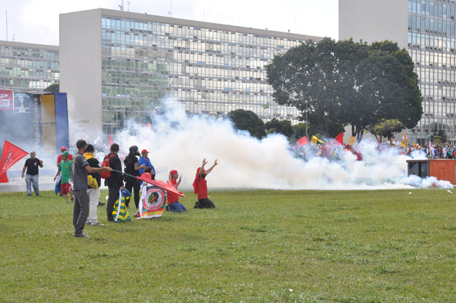 Imagem mostra manifestantes ajoelhados em meio ao gás lacrimogênio que tomou conta da Esplanada