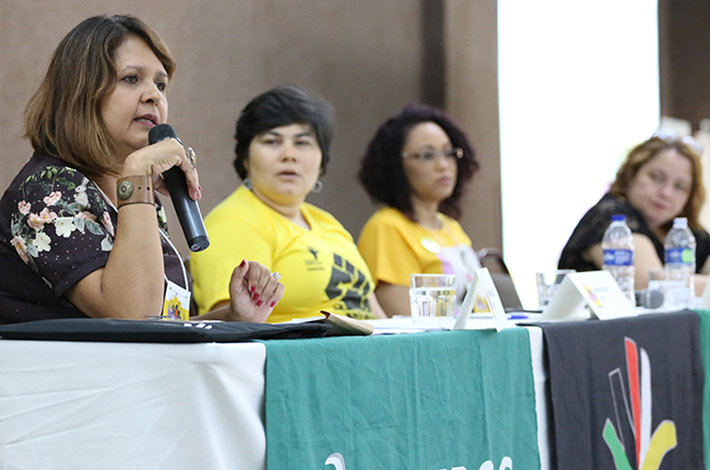 Fotografia da palestrante Erivã Velasco (UFMT) em destaque, com suas colegas de mesa ao fundo. 