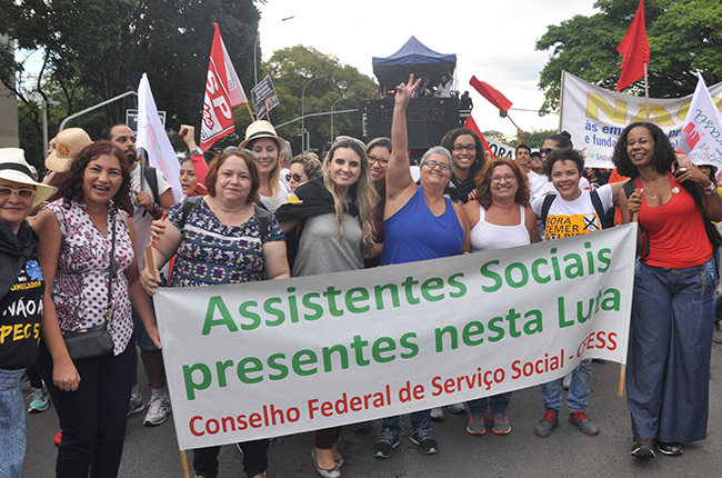 Foto mostra conselheiras do CFESS, assistentes sociais e professoras com a faixa 'assistentes sociais na luta'
