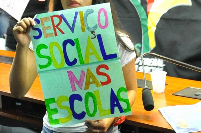 Imagem de uma estudante com o cartaz com os dizeres Serviço Social nas Escolas